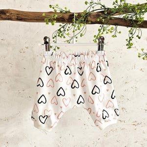 K&ouml;nnte beinhalten: Wei&szlig;e Baumwoll-Baby-Shorts mit einem rosa und schwarzen Herz-Druck.