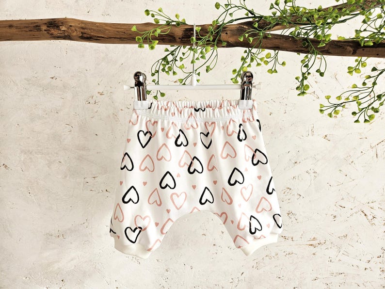 K&ouml;nnte beinhalten: Wei&szlig;e Baumwoll-Baby-Shorts mit einem rosa und schwarzen Herz-Druck.