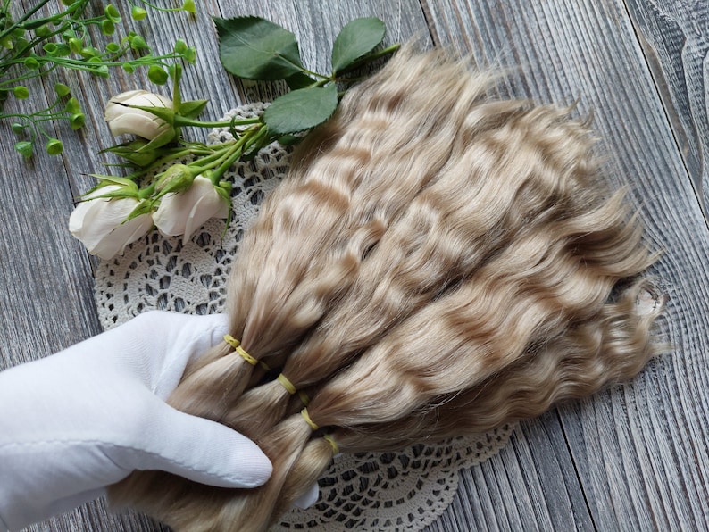 May include: Three bundles of wavy, light blonde human hair extensions. The hair is tied together with rubber bands.