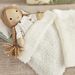 Close up of fabric doll sleeping with soft miniature blanket and pillow, doll bedding