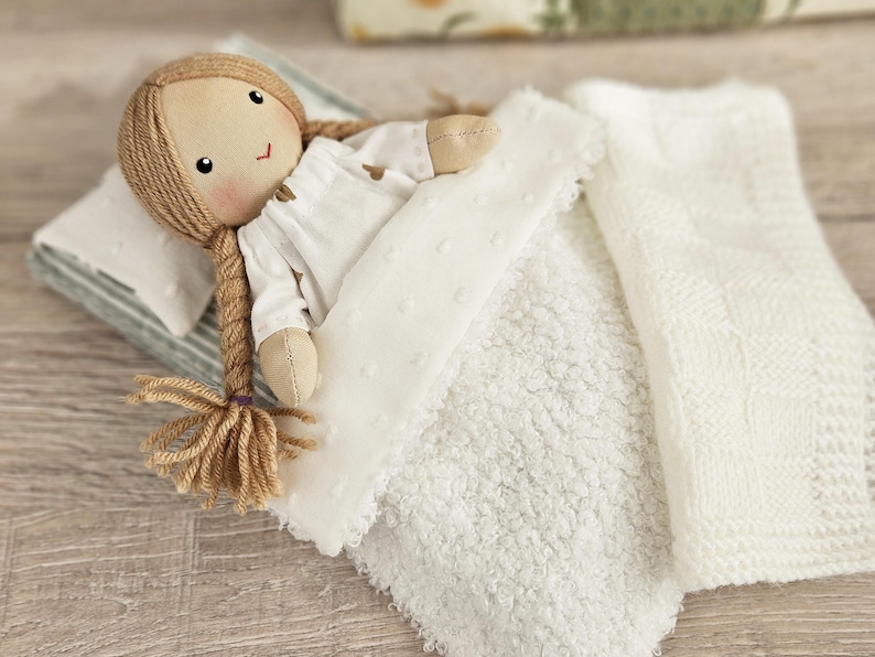 Close up of fabric doll sleeping with soft miniature blanket and pillow, doll bedding