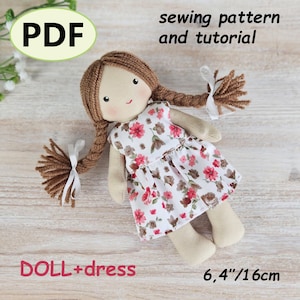 Puede incluir: Una muñeca de tela hecha a mano con trenzas de hilo marrón y un vestido floral. La muñeca mide aproximadamente 16 cm de altura. La imagen incluye el texto "PDF", "patrón de costura y tutorial" y "DOLL+dress".