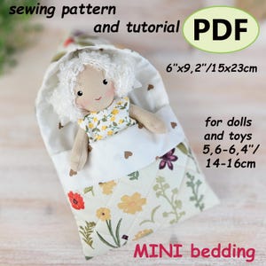 May include: A handmade doll in a mini bedding set. The doll has white curly hair and a floral dress. The bedding is white with brown heart accents and a floral patterned quilt. The set measures approximately 15cm x 23cm. The text says "MINI bedding".