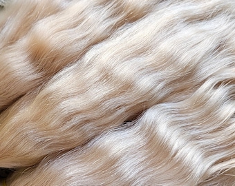 Puede incluir: Primer plano de un paquete de extensiones de cabello humano rubio claro. El cabello es ondulado y parece muy suave y sedoso.