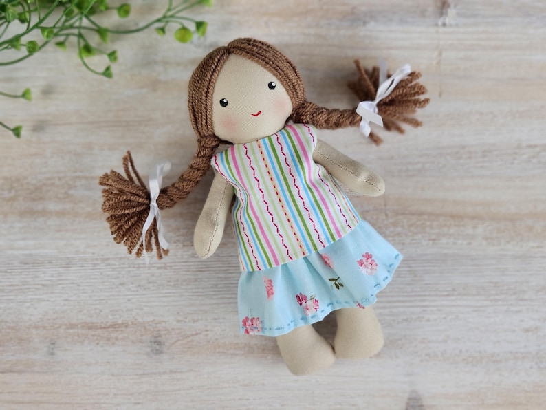Handmade cloth doll wearing striped top and blue floral skirt outfit made from sewing pattern