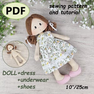 May include: A handmade doll with brown yarn hair, wearing a floral dress, pink shoes, and underwear. The image includes a smaller doll illustration and text that reads "PDF sewing pattern and tutorial". The doll is approximately 25 cm tall.
