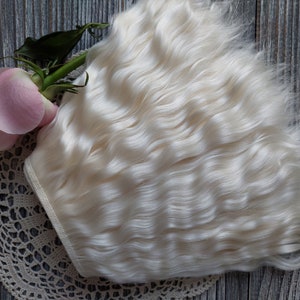 May include: A bundle of wavy, off-white hair extensions. A pink rose and a cream-colored lace doily are also in the image. The hair is styled in loose waves, and the overall aesthetic is soft and delicate.