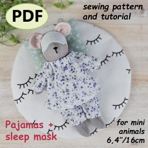 Op de afbeelding: Een handgemaakte muispop met pyjama en slaapmasker, rustend op een kussen. De pop draagt een outfit met bloemenprint. De afbeelding bevat de tekst "PDF", "naaipatroon en tutorial", "Pyjama's + slaapmasker" en "voor mini dieren 16cm".