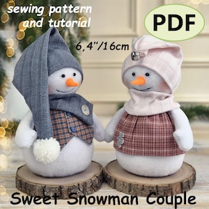 May include: A sewing pattern and tutorial for a Sweet Snowman Couple measuring 6.4 inches. Two plush snowmen with orange noses, one wearing a grey ribbed hat and plaid vest, the other in a pink ribbed hat and plaid dress with a silver bell.