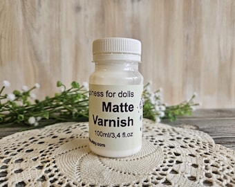 May include: A small white bottle of matte varnish for dolls. The bottle is labeled "Happiness for dolls Matte Varnish 100ml/3.4 fl.oz. etsy.com"