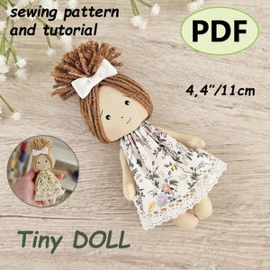 May include: A handmade tiny doll with brown yarn hair, a white bow, and a floral dress. The doll is approximately 4.4 inches (11 cm) tall. The image includes the text "sewing pattern and tutorial" and "Tiny DOLL".