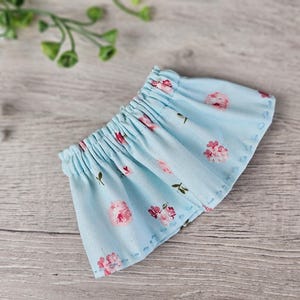 Blue floral doll skirt sewing piece shown flat with hand-stitched hem details