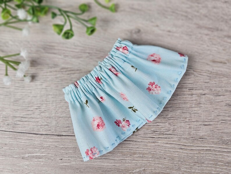 Blue floral doll skirt sewing piece shown flat with hand-stitched hem details