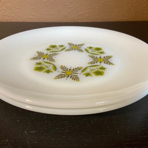 Puede incluir: Dos platos de cerámica blanca con un diseño floral verde y amarillo. Los platos están apilados uno encima del otro.