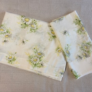 Puede incluir: Dos fundas de almohada de algodón blanco con un patrón floral de pequeñas margaritas blancas y hojas verdes.