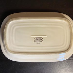 May include: Off-white rectangular stoneware serving platter. The underside of the platter is visible, with a recessed center and a raised border. The Noritake Stoneware logo is printed in black near the center.