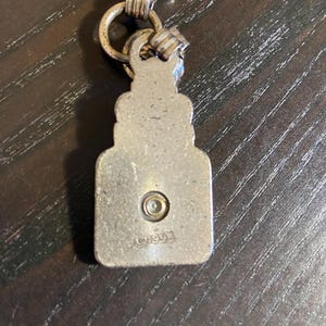 May include: A silver-toned metal pendant with a rectangular shape and a decorative top, connected to a chain with multiple rings. The pendant has a small circular detail and the text "CHOO93" is visible.