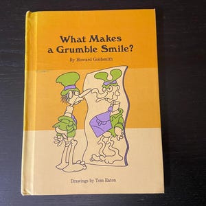 Puede incluir: Un libro infantil vintage titulado "What Makes a Grumble Smile?" de Howard Goldsmith. La portada presenta ilustraciones de dos personajes de dibujos animados con atuendo verde y morado. El libro tiene una cubierta amarilla y beige.