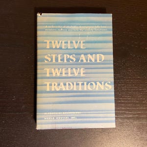 May include: A book titled "Twelve Steps and Twelve Traditions" with a light blue and white striped cover. The book is published by Alcoholics Anonymous World Services, Inc.