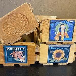 Puede incluir: Una pila de pequeñas cajas de madera desgastadas. Una caja tiene un diseño estampado que dice "Napa Valley Box Company". Otras cajas presentan etiquetas coloridas con imágenes de una mujer nativa americana, una flor de pascua y un girasol.