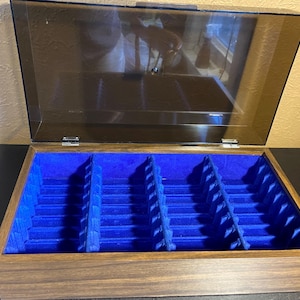 May include: A wooden jewelry box with a hinged, transparent lid. The interior is lined with bright blue velvet and divided into several compartments. The box has a dark brown finish and is open, revealing the interior.