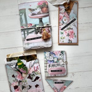 Puede incluir: Una colección de manualidades en papel hechas a mano con diseños florales y de mariposas. Incluye un diario, un marcapáginas y tarjetas con citas inspiradoras como "a dream is a wish your heart makes" y "love yourself first."