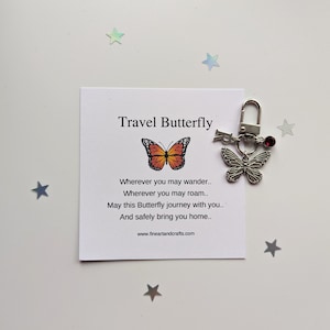 May include: A silver travel butterfly keychain with a red crystal charm and a small butterfly charm. The keychain comes with a card that reads "Travel Butterfly" and a poem about safe travels.