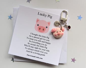 May include: A white card with the text "Lucky Pig" and a pink pig illustration. The card includes a poem about a lucky pig charm. The charm is a small pink pig with a silver keyring and a red crystal charm.