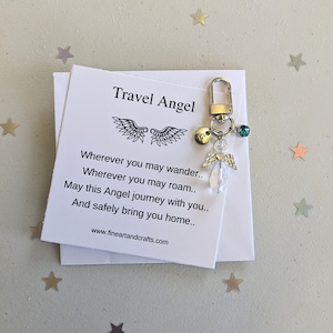 Könnte beinhalten: Ein silberner Reiseengel-Schlüsselanhänger mit einem Kristall-Anhänger und einem kleinen silbernen Anhänger mit dem Buchstaben G. Der Schlüsselanhänger wird mit einer Karte geliefert, auf der "Reiseengel" steht, und einem Gedicht über die Reise des Engels mit dir.