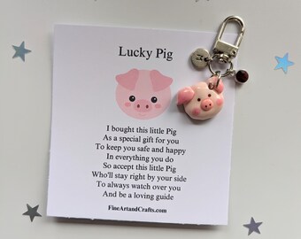 May include: A pink pig keychain with a silver charm and a red bead. The keychain comes with a card that reads "Lucky Pig" and a poem about the pig being a lucky charm.
