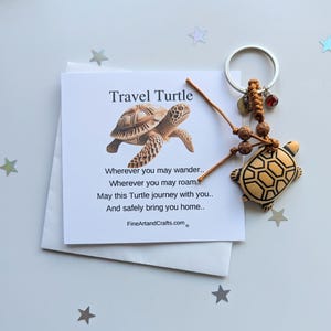 May include: A wooden turtle keychain with a brown and beige shell. The keychain is attached to a brown cord with wooden beads and a silver key ring. A small card with the text "Travel Turtle" and a poem about safe travels is included.