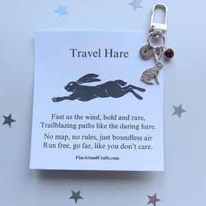 Puede incluir: Un llavero de plata con un dije de una liebre corriendo, un dije de plata con la letra V y una cuenta de cristal roja. El llavero viene con una tarjeta que dice "Travel Hare" y un poema sobre una liebre corriendo libre.