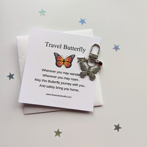 May include: A silver travel butterfly keychain with a red gem. The keychain comes with a card that reads "Travel Butterfly" and a poem about the butterfly's journey.