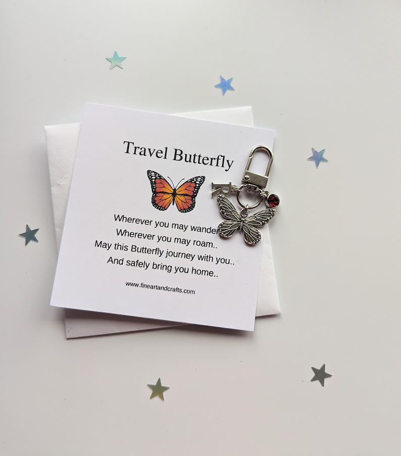 May include: A silver travel butterfly keychain with a red gem. The keychain comes with a card that reads "Travel Butterfly" and a poem about the butterfly's journey.