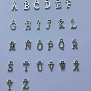 May include: Silver alphabet letter charms, A through Z, with a loop at the top for attaching to jewelry or other crafts.