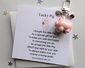 May include: A pink pig keychain with a silver clasp and a small red gem. The keychain is attached to a white card with the text "Lucky Pig" and a poem about safety and happiness.