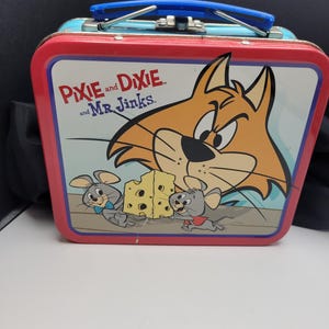 May include: Vintage metal lunchbox featuring the cartoon characters Pixie, Dixie, and Mr. Jinks. The lunchbox has a red frame, a light blue top, and a blue handle. The front panel displays a cartoon cat, two mice, and a block of cheese.