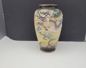 May include: A small, yellow and grey ceramic vase with a dragon design. The dragon is painted in silver, blue, and white. The vase has a brown rim.