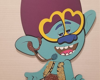 May include: A blue troll character with purple hair, wearing yellow sunglasses and a brown vest with gold glitter. The troll is holding a microphone and has a big smile.