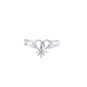 May include: A silver ring featuring a heart-shaped design with a small starburst at the bottom. The ring has a small, light green gemstone in the center of the starburst and two clear gemstones on the heart. The ring is set against a white background.