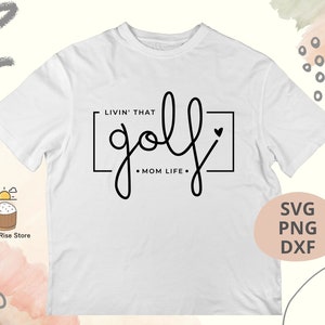 May include: White t-shirt with black text that says "Livin' that golf Mom Life" with a heart symbol.