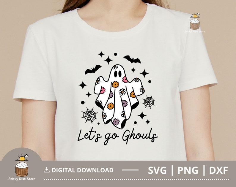 Pu&ograve; includere: Maglietta bianca con un'illustrazione in bianco e nero di un fantasma con motivi floreali. Il testo "Let's go Ghouls" &egrave; stampato sotto il fantasma.