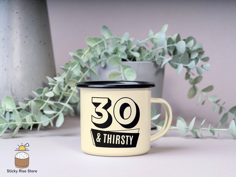 May include: Cream-colored enamel mug with a black rim and handle. The mug features the text "30 & THIRSTY" in a bold, black font. The mug is likely used for beverages and is a humorous gift for someone turning 30.