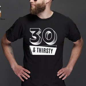 May include: Black t-shirt with the text "30 & Thirsty" in white. The number "30" is in a 3D style, and the text is on a white banner. The shirt is a crew neck style.