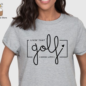 May include: Gray t-shirt with the text "Livin' that golf - Mom Life -" in a black square with a small heart.