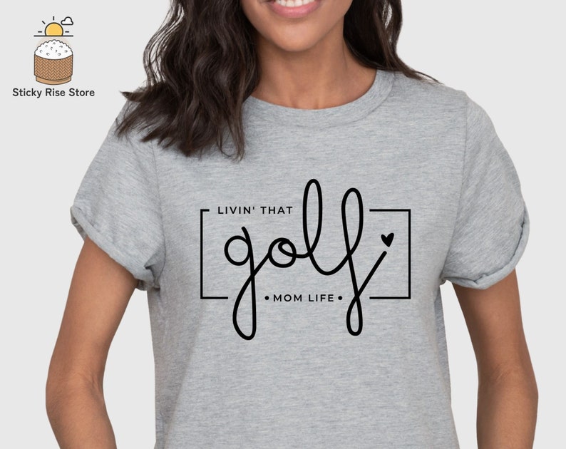 May include: Gray t-shirt with the text "Livin' that golf - Mom Life -" in a black square with a small heart.