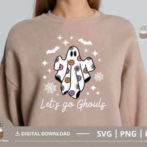 Pu&ograve; includere: Una felpa color beige con un disegno di un fantasma e il testo "Let's go Ghouls". Il fantasma &egrave; bianco con fiori rosa, viola e gialli. Il design &egrave; perfetto per Halloween.