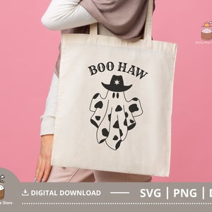 Puede incluir: Una bolsa de tela blanca con texto negro que dice "BOO HAW" y un fantasma de estampado de vaca blanco y negro con un sombrero de vaquero.