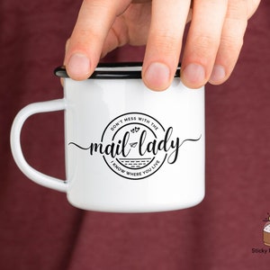 May include: White enamel mug with a black rim and handle. The mug has a black and white graphic that says "Don't mess with the mail lady I know where you live".