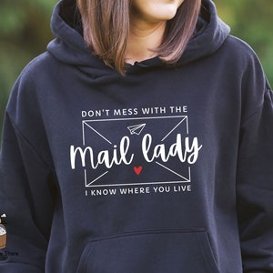 May include: A dark blue hoodie with a white graphic that says "Don't mess with the mail lady I know where you live". The graphic is in the shape of an envelope with a paper airplane inside.